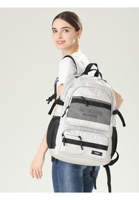 Zaino grigio e nero con numerosi scomparti, dettagli in rete, spallacci regolabili e tasche frontali con zip. Tessuto morbido.