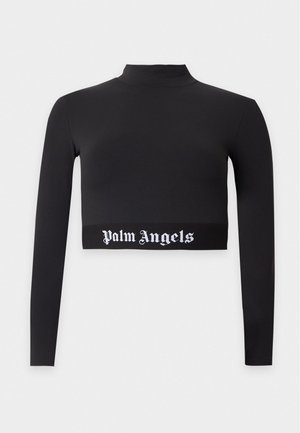 Osoba nosząca czarną, długą crop top z napisem "Palm Angels", czarne spodnie typu cargo, białe sneakersy i ciemne okulary przeciwsłoneczne, stojąca na jednolitym tle.