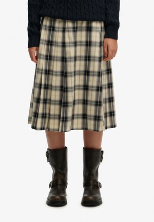 Jupe à carreaux marron clair et noir avec des plis, associée à des bottes mi-mollet marron foncé avec des boucles et une finition texturée.