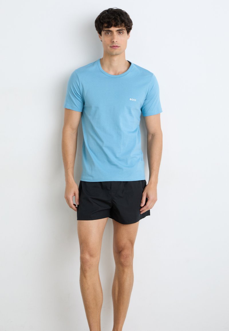 Lyseblå bomull t-skjorte med rund hals, korte ermer og en liten hvit logo på brystet; kombinert med svarte shorts.