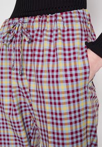 Pantalons à motif à carreaux comportant des carrés rouges, bleus, jaunes et blancs. Taille élastique avec cordons ajustables et poches latérales.