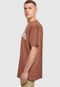 Brun bomulds t-shirt med korte ærmer, med et hvidt trykt design på forsiden og en klassisk afslappet pasform.