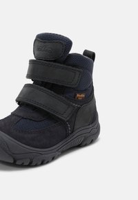 Bota infantil de color azul marino que combina material de ante y malla, equipada con dos correas de Velcro ajustables y una suela de goma texturizada.