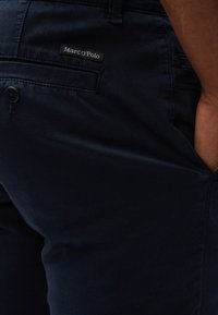 Pantalons bleu marine en tissu doux, avec une poche arrière portant une étiquette noire indiquant "Marc O'Polo" et une fermeture à bouton.