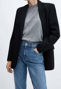 Black blazer with structured lapels, worn over a gray sweater. Paired with high-waisted blue denim jeans. Smooth fabric and tailored fit.