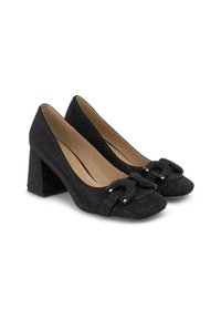 Zapatos de tacón negro con un upper texturizado, que cuentan con un detalle de lazo y pequeños acentos negros. El diseño de tacón ancho proporciona estabilidad.