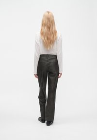 Black high-waisted leather pants with a straight-leg design, smooth texture, and back pockets, paired with a white long-sleeve top.