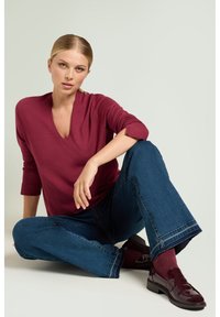 Bordeauxrode V-hals trui met driekwartmouwen, gecombineerd met wijde blauwe denim jeans en glanzende bordeauxrode loafers.