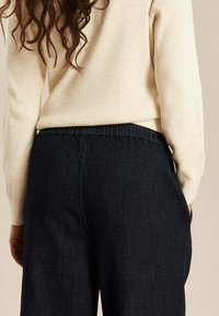 Donkerdenim wijde broek met een elastische tailleband, gecombineerd met een crèmekleurige geribde trui. De stof lijkt soepel, met subtiele stikdetails.