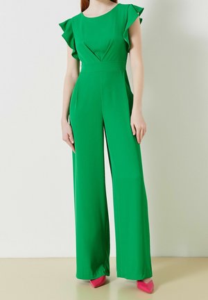 Combinaison verte avec des manches courtes à volants, un corsage ajusté et un pantalon large. Texture lisse, couleur unie et design minimaliste.