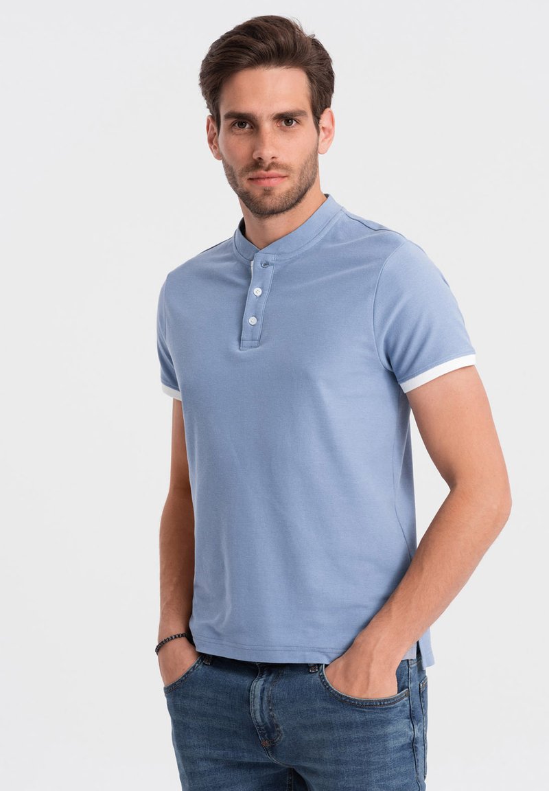 Svetle modrý polo tričko s krátkým rukávem, límečkem, třemi knoflíky a bílými manžetami. Kombinováno s úzkými modrými džíny.