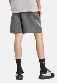 Grå atletiske shorts med en struktureret stof, der har reflekterende detaljer og en løs pasform. Båret med sorte sokker og sneakers.