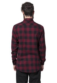 Camicia flanellata a quadri rossi e neri, maniche lunghe, colletto con bottoni, orlo leggermente curvo, texture morbida e grande motivo a scacchi contrastante.