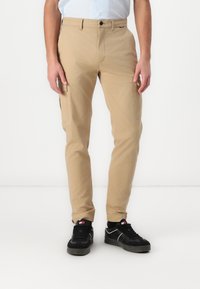 Beige chinos met een slim fit, voorzien van zijzakken en een knoopsluiting. Gediend met zwarte sneakers en opvallende sokken.