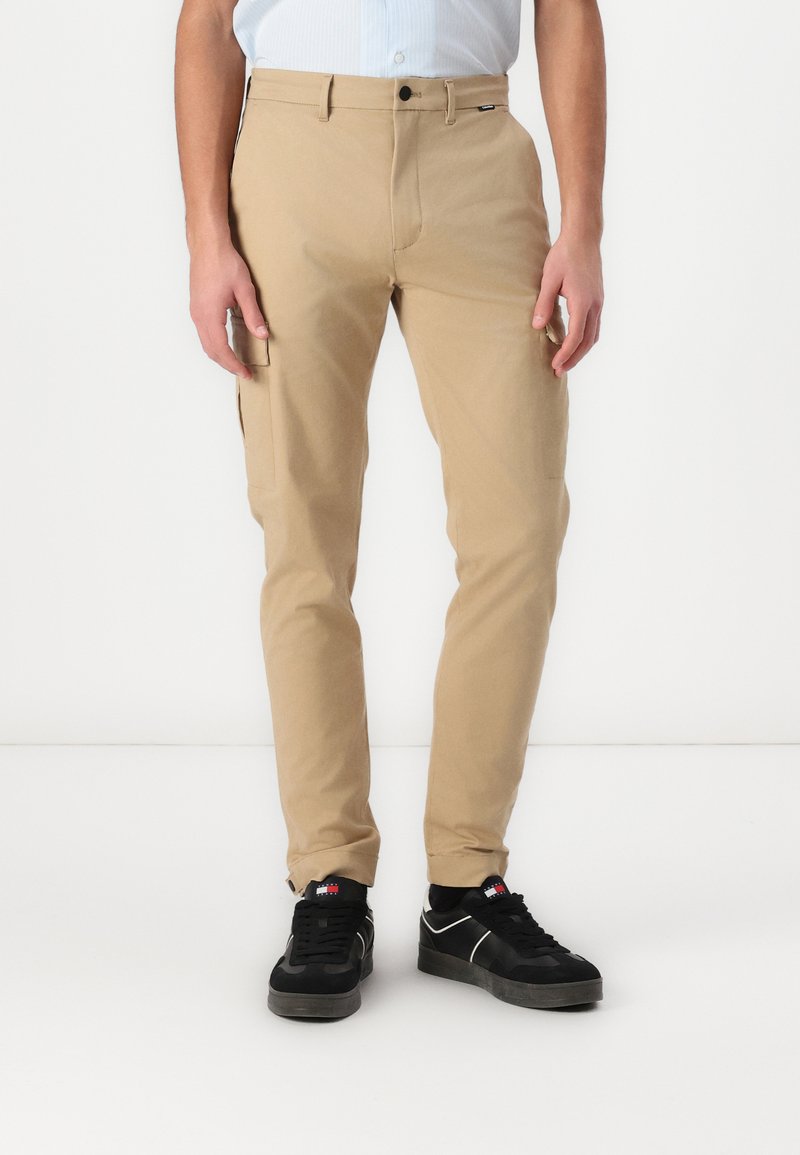 Beige chinos met een slim fit, voorzien van zijzakken en een knoopsluiting. Gediend met zwarte sneakers en opvallende sokken.