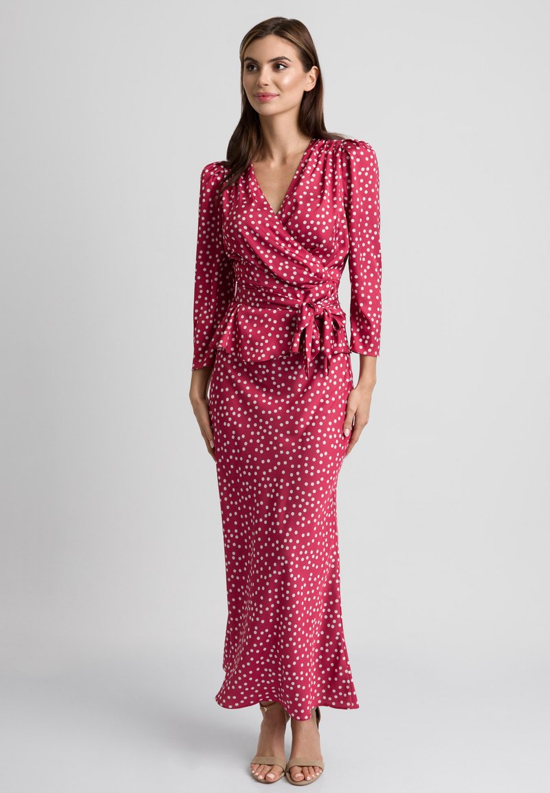 Długa sukienka typu wrap w różowym materiale w białe kropki, z długimi rękawami, wiązanym w pasie oraz dopasowanym krojem. Gładka tekstura.