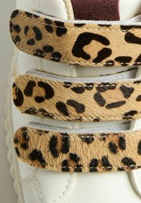 Witte sneaker met drie leoprintbanden. De banden hebben een gestructureerd, zacht vachtachtig materiaal met zwarte vlekken op een tan achtergrond.