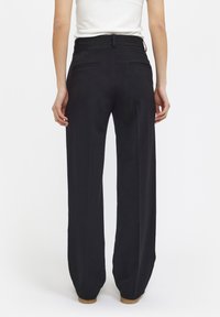 Zwarte wijde broek van gladde stof. Heeft een hoge taille, twee achterzakken en een getailleerde pasvorm. Subtiele plooidetails langs de benen.