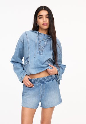 Blå denimkort hoodie med snörning i halsen och två framfickor, ihopparad med blå högmidjade shorts med elastisk midja.