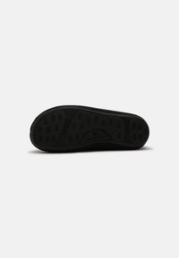 Black rubber shoe sole with a textured surface featuring circular grip patterns and a rounded toe. The brand name is embossed.