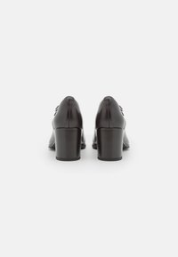 Scarpe con tacco alto in pelle nera, con una finitura liscia e punta arrotondata, dotate di un tacco a blocco modesto e di eleganti dettagli a fiocco sui lati.