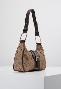 Brown monogram-patterned handbag with dark brown adjustable strap and gold-tone buckle detail on a white pedestal.
