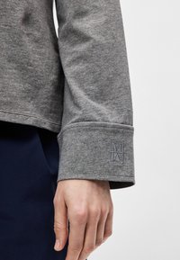 Γκρι μακρυμάνικο μπλουζάκι με διπλωμένο μανίκι και κεντημένο λογότυπο στο μανίκι. Λείο υλικό με χαλαρή εφαρμογή.