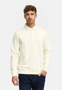 Langermet polo skjorte i lys gul, med krage og knapper, teksturert stoff og avslappet passform. Sammen med mørke jeans.