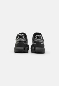 Pair of black athletic shoes with chunky soles viewed from the back on a white background, featuring reflective accents and branding.