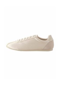 Beige sneaker with smooth synthetic upper and soft suede heel accent. Round toe, lace-up design, and low-profile rubber sole.