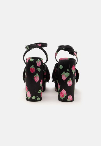 Sandales noires à talons hauts avec motifs de roses roses, talons blocs épais et brides de cheville avec boucles argentées, vues de dos sur fond blanc.