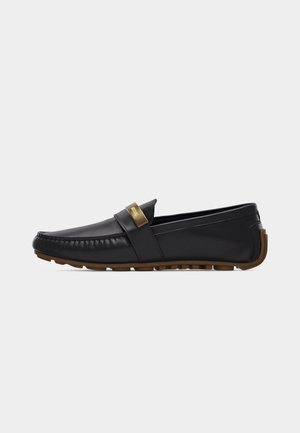 Black leather loafer with brown sole and gold metal accent on strap, side view, against a plain white background.