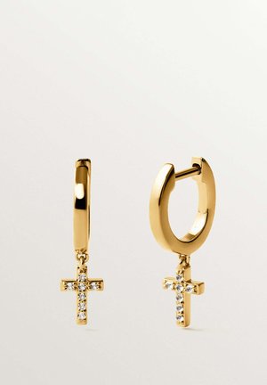 Pendientes de aro dorado con pequeños colgantes en forma de cruz adornados con piedras preciosas transparentes, colgando sobre un fondo claro.