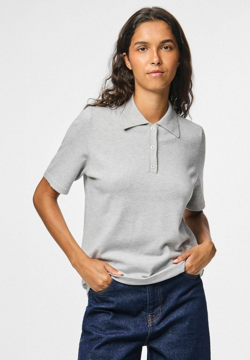 Pilkas polo marškinėliai su apykakle, trumpomis rankovėmis ir trimis mygtukų padėtimis. Dėvimi su tamsiai mėlynomis džinsinėmis kelnėmis. Sklandus tekstūra, kasdienis dizainas.