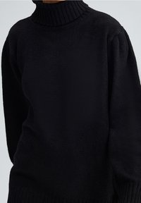 Czarny sweter z golfem wykonany z miękkiego materiału; ma prążkowany dekolt i mankiety, luźny krój oraz teksturowane wykończenie.