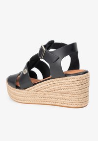 Sandalia de cuña de cuero negro con plataforma de yute trenzado, diseño con cortes, correa de tobillo ajustable y detalles en hardware plateado.