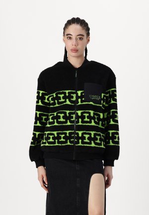Black fleece bomber jacket with bright green geometric pattern, zip closure, ribbed cuffs, and front pocket. Textured finish overall.