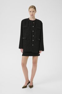 Černá tweedová bunda s kulatým výstřihem, dvěma předními kapsami a stříbrnými knoflíky. Nosená přes ladící černou mini sukni a zelené lodičky.