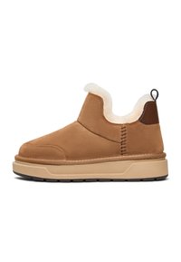 Brune ruskind slip-on sko med hvid faux pelsforing, en kontrasterende brun hælaccent og en klodset beige sål med et mønstret dæk.