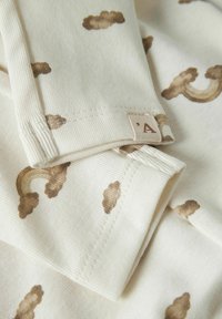 Kreemivärviline puuvillane kangas, millel on pruunid pilved ja vikerkaare mustrid. Omab ribakoe tekstuuri, rullitud ääri ja väikest sildikest, millel on 'A' logo.