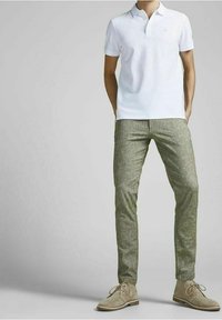 Biała koszulka polo z klasycznym kołnierzykiem, zestawiona z jasnozielonymi, teksturowanymi, dopasowanymi spodniami oraz beżowymi zamszowymi butami.