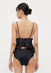 Melnas satīna apakšveļas komplekts ar mežģīņu apdari un ruffles detaļām, kā arī atbilstošiem augstās jostasvietas apakšbiksēm, kas izceļ elegantu dizainu.