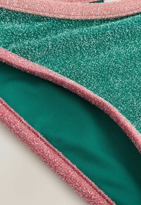 Grön texturerad tyg med silvertrådar, kantad med en rosa texturerad kant. Har ett smidigt innerfoder i solidgrön.