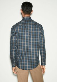 Camisa de hombre de manga larga en patrón de cuadros azul y gris, con cuello puntiagudo y dobladillo curvado, hecha de una tela suave.