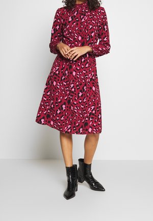Robe à manches longues à motif léopard rose et noir, avec une taille cintrée, une jupe fluide et des bottines en cuir verni noir.