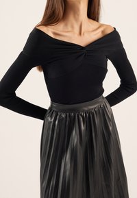 Haut noir à manches longues côtelé avec encolure décolletée, associé à une jupe plissée en similicuir noir avec une taille élastique.