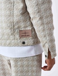 Beige mønstret jakke med diamantmotiver, quiltet tekstur og et brunt lædermærke. Hvid skjorte under, afsluttet med sorte knapper.