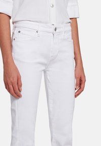 Hvide denimjeans med slim fit, fem-lomme design og sølvfarvede detaljer ved taljen og lommerne. Glat tekstur.