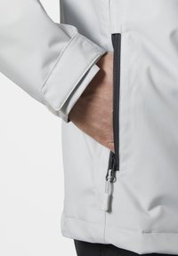 Giacca leggera bianca con tasca con zip e polsini regolabili. Texture liscia con sottili righe verticali e una zip a contrasto.
