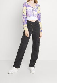 Cropped tie-dye top in purple and yellow with long sleeves; paired with black cargo pants featuring front pockets and a zip closure.
